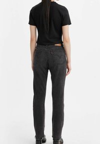 Camiseta negra de manga corta combinada con vaqueros de tiro alto gris. Características notables incluyen una etiqueta de cuero y un dobladillo deshilachado.