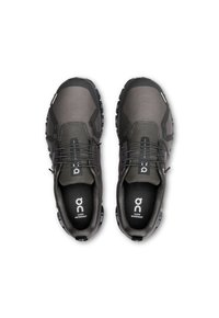 Chaussures noires imperméables avec une tige texturée, au design minimaliste, avec un système de laçage et une semelle robuste, arborant un logo sur la semelle intérieure.