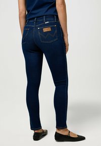 Jeans skinny bleu foncé, en denim, avec une taille haute, des poches arrière avec un détail de couture et une étiquette en cuir.