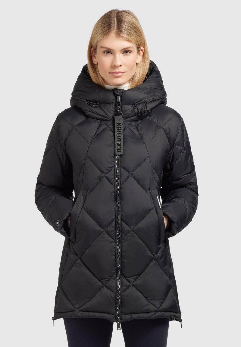 Doudoune noire avec un design matelassé, col montant et fermeture éclair. Dispose de poches latérales et d'une capuche amovible. Matière synthétique lisse.