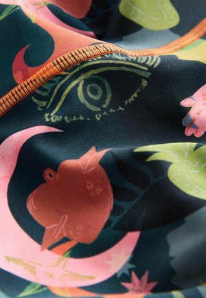 Multicolored fabric featuring abstract floral and eye patterns. Neat orange stitching along the edges adds contrast to the dark background.