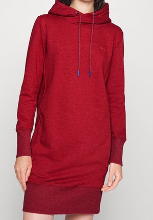 Vrouw draagt een rode hoodie-jurk met lange mouwen tot op de knie, voorzien van voorste trekkoorden en geribbelde boorden en zoom.
