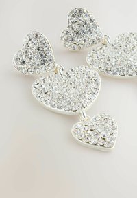 Silberne, herzförmige Ohrringe, verziert mit zahlreichen klaren Strasssteinen, mit einem Design aus drei Herzen, die durch Metallverbindungen verbunden sind.