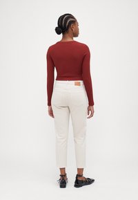 Maroon long-sleeve top, cream cropped pants with frayed hem, black patent flats, back view, textured hair styled in a bun.