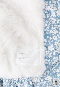 Morbido pelliccia sintetica bianca accanto a un tessuto blu con un motivo floreale bianco. Presenta un'etichetta con spazi per "NOME" e "TELEFONO."