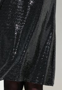 Vestido negro con pedrería que presenta una superficie texturizada con lentejuelas brillantes esparcidas, un diseño fluido y un dobladillo a la altura de la rodilla.