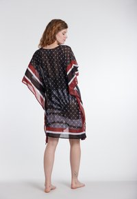 Prozoren črn kaftan z geometrijskim vzorcem, širokimi rokavi in rdečimi črtami ob robovih, ohlapen kroj in lahka tekstura.