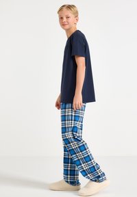 T-shirt bleu marine à manches courtes, pantalon de pyjama à carreaux bleu et blanc, chaussons beiges en peluche ; coupe décontractée, tissu doux, design casual.