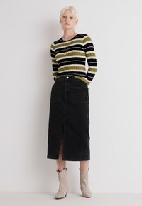 Jupe en denim noir avec fente à l'avant, associée à un pull côtelé rayé vert et noir. Les chaussures incluent des bottines beiges à la cheville.