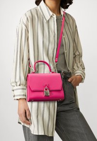 Sac à main en cuir rose à forme structurée, avec une poignée supérieure, une bandoulière amovible, une ferrure argentée et une fermeture à clip.