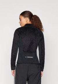 Must kiu spordijakk, millel on tekstuuriga kangas õlgadel, siledad küljed ja sobiv disain. Tagaküljel on must logoteip.