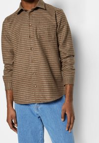 Ruskea ja kerma ruudullinen paita, jossa on napitettavat kaulukset, pitkät hihat, etunapit ja yksi rintatasku, valmistettu pehmeästä kankaasta.