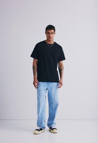 Black cotton t-shirt with short sleeves, paired with light blue denim jeans. Black and white sneakers complete the outfit. Simple design, no patterns.