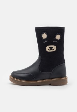 Botte noire pour enfants avec semelle marron, présentant un motif de visage d'ours avec des oreilles et des yeux fermés sur la partie supérieure.