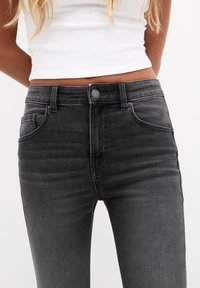 Jeans de mezclilla negra con un diseño ajustado, estilo de cinco bolsillos, cierre frontal con botón y un ligero desgaste que aporta textura y detalle.