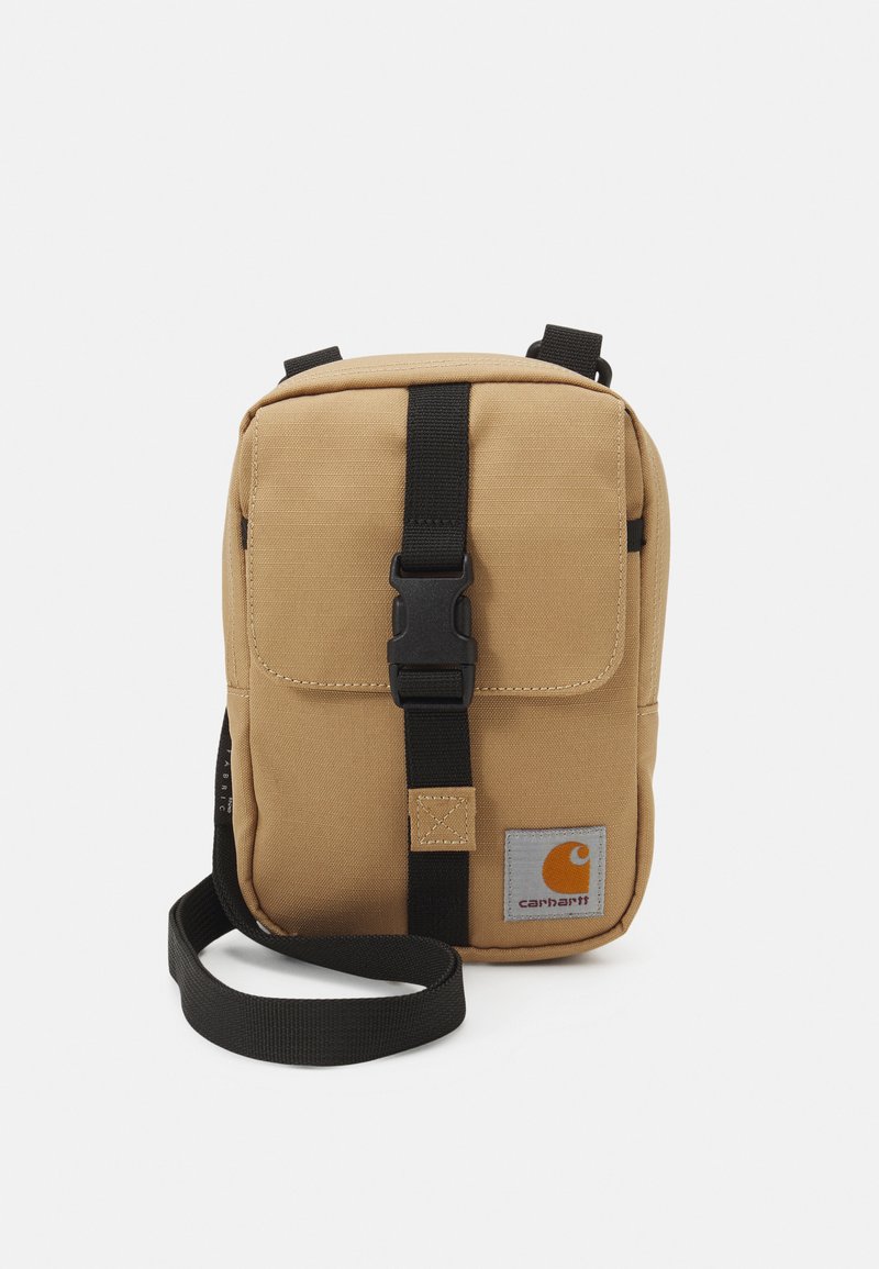 Bolsa transversal de canvas em tom bege, com uma alça preta, aba frontal com fivela e um logótipo visível em laranja e cinza. Design compacto.