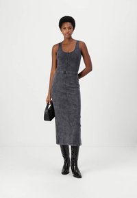 Rochie midi din denim gri cu un corp ajustat, fermoar central și detalii la talie. Modelul poartă cizme negre până la genunchi și ține o geantă mică neagră.