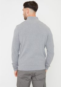Maglione grigio lavorato a maglia con collo alto, polsini e orlo a coste. Visualizzato da dietro, mostra la sua texture liscia e il design aderente.