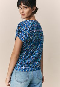 Blouse bleu à motifs floraux rouges et verts, à manches courtes et coupe décontractée, associée à un denim délavé.