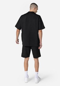 Black textured short-sleeve shirt and shorts set, featuring a relaxed fit. Worn with white sneakers and ankle-length socks.