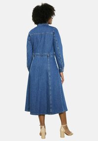 Džinsu kleita ar garām piedurknēm, ar akcentētu vidukli un plūstošu A-silueta svārku. Aprīkota ar zilu audumu, kontrastējošām šuvēm un pogājamām piedurknēm.