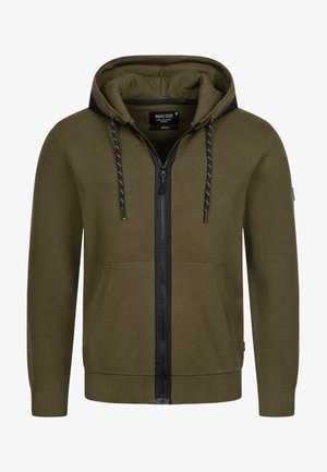 Felpa con zip verde oliva con dettagli neri, lacci e tasche a marsupio. Realizzata in materiale a coste con tessuto testurizzato.