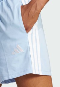 Shorts de sport bleu clair avec des rayures blanches sur les côtés et un logo brodé blanc. Tissu doux avec poches et coupe décontractée.