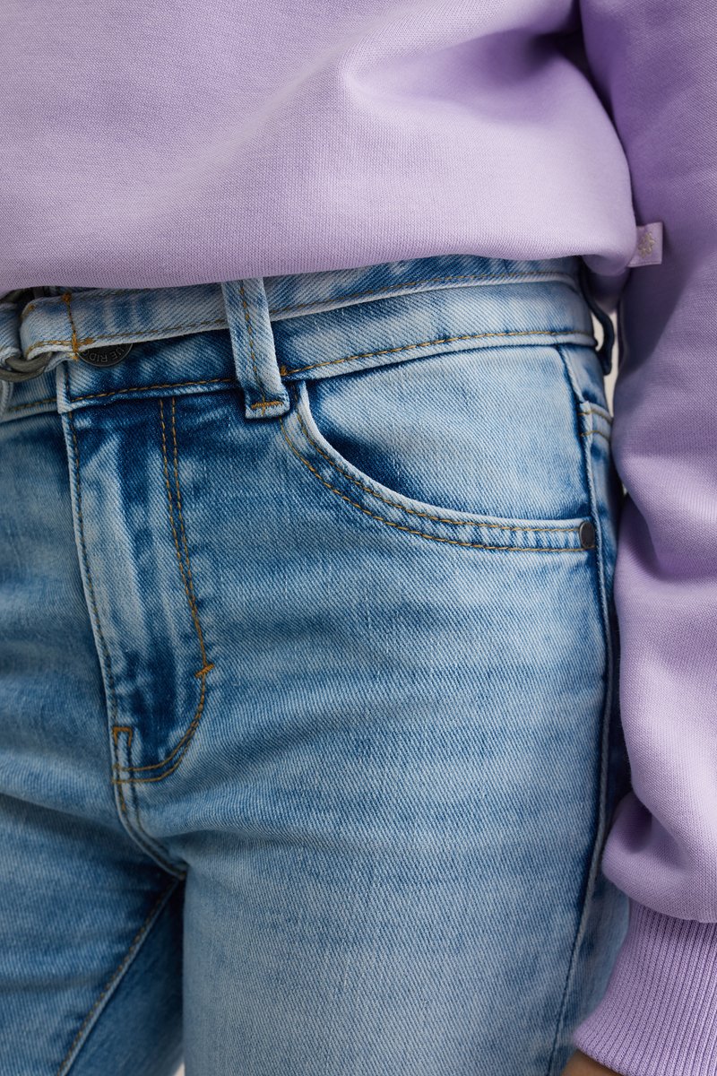 Hele sinise teksade vöökoht ja tasku, millel on oranž õmblus, lähivõte; paremal paistab lilla kampsuni varrukas.