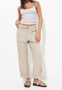 Pantalons beige à jambes larges avec deux poches avant et une ceinture. Associés à un débardeur blanc à rayures grises et des sandales à pois.