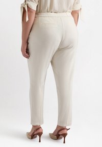 Jasnobeżowe, zwężane spodnie charakteryzują się gładką fakturą, elastyczną talią i tylnymi kieszeniami. Połączone z jasnymi, szpiczastymi szpilkami.