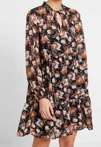 Robe à manches longues à motif floral sur fond noir, ornée de fleurs roses, blanches et oranges, avec un décolleté à ouverture centrale avec lien et un ourlet à volants.