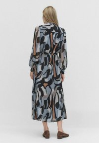 Lang geschnittenes, plissiertes Kleid aus einem leichten Stoff mit einem abstrakten Muster in Schwarz, Beige, Blau und Brauntönen; elastischer Taillenbund, lange Ärmel.