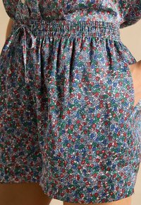 Kvetinové šortky s naťahovacím pásom, bočnými vreckami a živými farbami vrátane červenej, modrej a zelenej na svetlom pozadí.