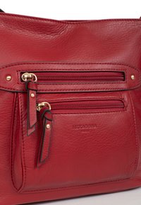 Borsa a tracolla in pelle rossa con una finitura testurizzata. Presenta due tasche con cerniera, hardware color oro e branding impresso. Design complessivamente strutturato.