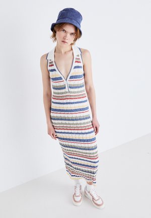 Abito lavorato a maglia, senza maniche, multicolore con righe orizzontali in blu, verde, rosso e giallo; presenta un profondo scollo a V e una texture a costine. Abbinato a sneakers.