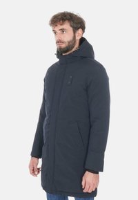 Cappotto imbottito blu navy con cappuccio, dotato di zip frontale, due tasche laterali e una texture liscia. Dettaglio a bottone sul petto.