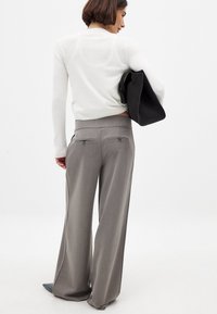 Pantalones de pierna ancha en gris claro con bolsillos traseros con cremallera, combinados con un suéter de punto ajustado blanco y un bolso negro. Textura de tela suave.