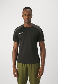 Camiseta deportiva negra de Nike con cuello redondo, mangas cortas y acentos en gris en los hombros. Tejido texturizado para transpirabilidad y comodidad.