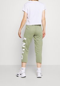 Vit kortärmad t-shirt med hoppade ärmar, kombinerad med ljusgröna joggingbyxor som har stor vit text "P R N T" på vänstra benet.