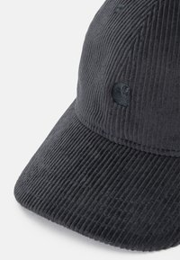 Gorra de pana negra con una textura acanalada, que presenta un logotipo bordado a juego en la parte frontal. La visera es plana y ligeramente curvada.