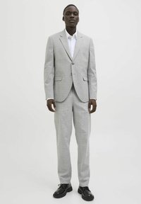 Traje gris a cuadros con corte entallado, chaqueta de un botón y pantalones a juego. Llevado con una camisa blanca de cuello y zapatos negros.