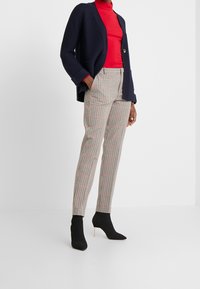 Cardigan blu navy con un bottone singolo, dolcevita rosso e pantaloni a quadri in beige, nero e rosso. Stivaletti neri alla caviglia completano il look.