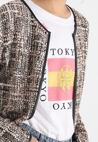 Marynarka tweedowa w kolorze różowym i czarnym z teksturowanym wzorem oraz czarnymi wykończeniami, noszona na białej koszulce z grafiką Tokio i kolorami.