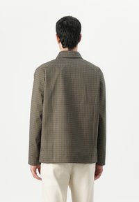 Checkered jacket in brown and beige tones, featuring a collar, long sleeves, and a relaxed fit. Textured fabric, back view displayed.