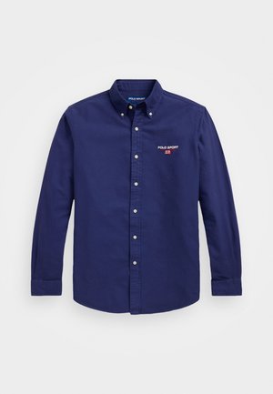 Tumedat sinise värvi nööbid alla särgid, mis on valmistatud puuvillast. Särgil on klassikaline krae, pikad varrukad ja rinnal väike broderitud "Polo Sport" logo.
