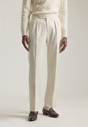 Pantalones plisados color crema fabricados en un tejido suave, con un corte entallado, bolsillos laterales y una textura lisa.