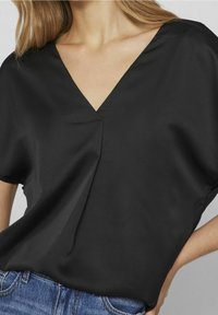 Blusa nera con scollo a V, maniche corte e una texture morbida e liscia. Ha una vestibilità ampia con dettagli di drappeggio delicati.