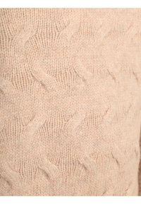 Cable-knit sweater in soft beige wool with a textured pattern and ribbed accents, featuring a thick, cozy appearance and substantial yarn.