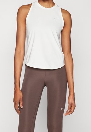 Athletische Person trägt ein ärmelloses weißes Top und braune Leggings mit hoher Taille, beide mit kleinen Nike Swoosh-Logos.