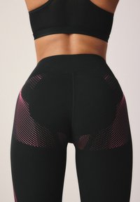 Svarta leggings med hög midja, utrustade med rosa prickiga accenter och texturerat mönster längs sidorna. Slät tygfinish.